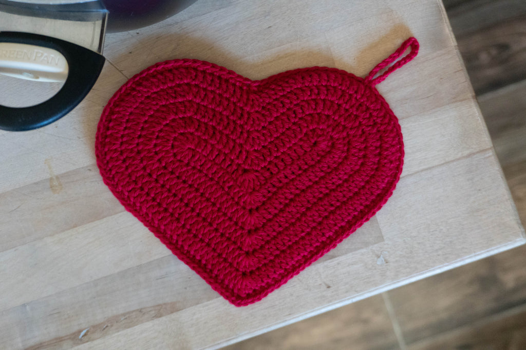 heart-shaped crochet hot pad used in kitchen setting